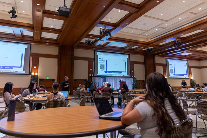 SDSU students attend a Google Gemini workshop inside Montezuma Hall, watching a live demo on multiple projection screens.
